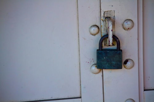 白い扉に掛かった緑色の錆びた南京錠と金具