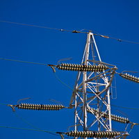 青空の下にそびえる白い送電鉄塔と電線の写真