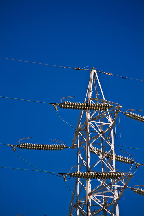青空の下にそびえる白い送電鉄塔と電線