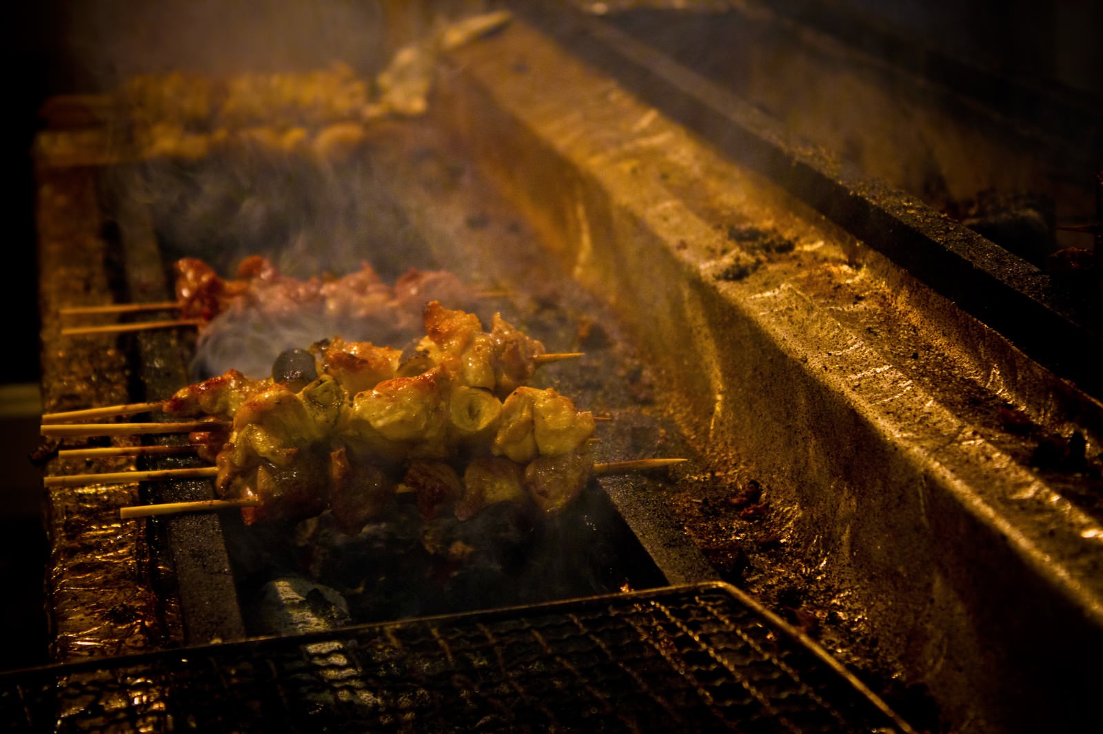 煙が立ち上る金属の網の上で焼く炭火の焼き鳥
