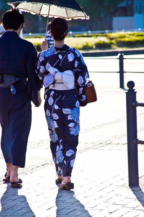 日傘をさしかごバッグを持つ浴衣の恋人の後ろ姿
