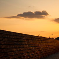 夕焼けに染まる雲とレンガの壁がある防波堤の写真