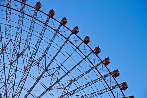 青空を背景に赤いゴンドラが並ぶ夕暮れの観覧車