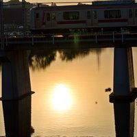 夕焼けの川に架かる鉄橋を渡る白と赤の電車の写真