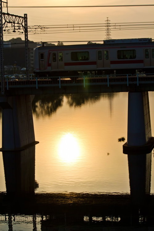 夕焼けの川に架かる鉄橋を渡る白と赤の電車