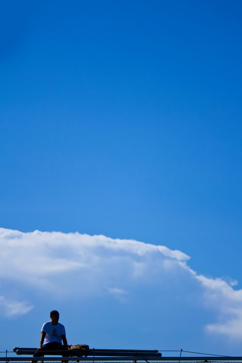 快晴の青空を背景に手すりに座る青年