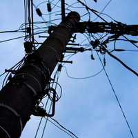 真下から見上げた電柱と電線が交差するシルエットの写真