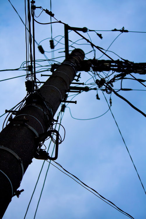 真下から見上げた電柱と電線が交差するシルエット