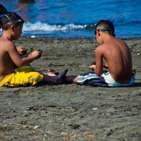 砂浜でゴーグルを付けて座る3人の浜辺の子供たちの写真