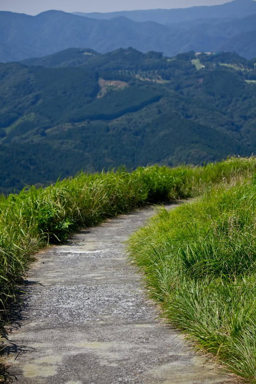 山々が連なる風景の中を曲がりながら続く小道