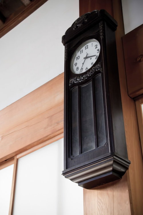 飾り彫りが施された古い木製の壁掛け振り子時計