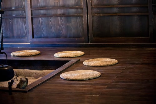 丸い編み敷物と黒い鉄鍋が並ぶ囲炉裏と座布団