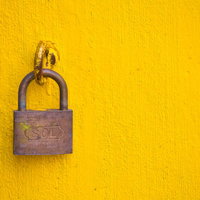 黄色い壁にSOLの文字が彫られた南京錠と鎖の写真