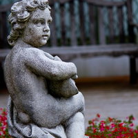 苔や汚れが付いた庭の子供の石像と花壇の花の写真