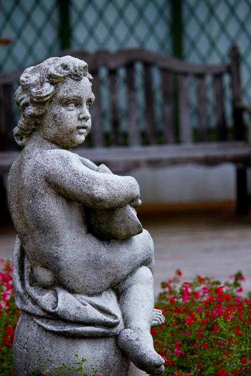 苔や汚れが付いた庭の子供の石像と花壇の花