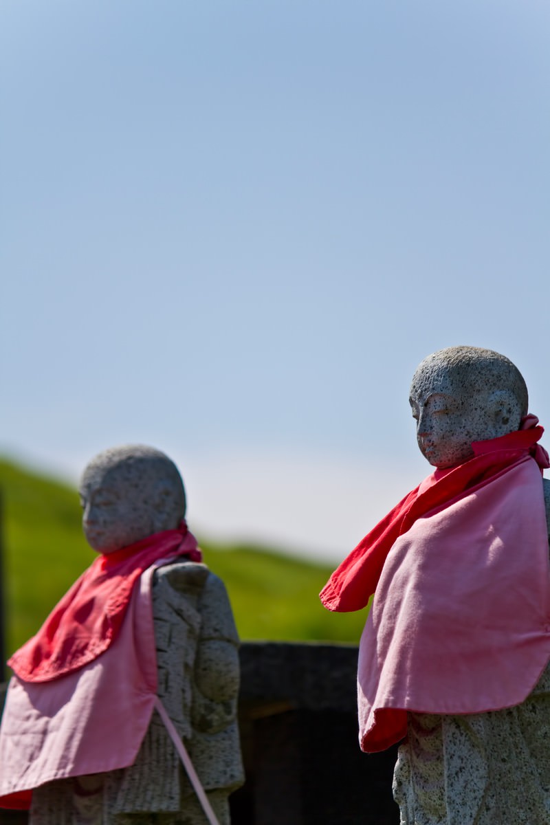 Two stone Jizo statues with red scarves under blue sky