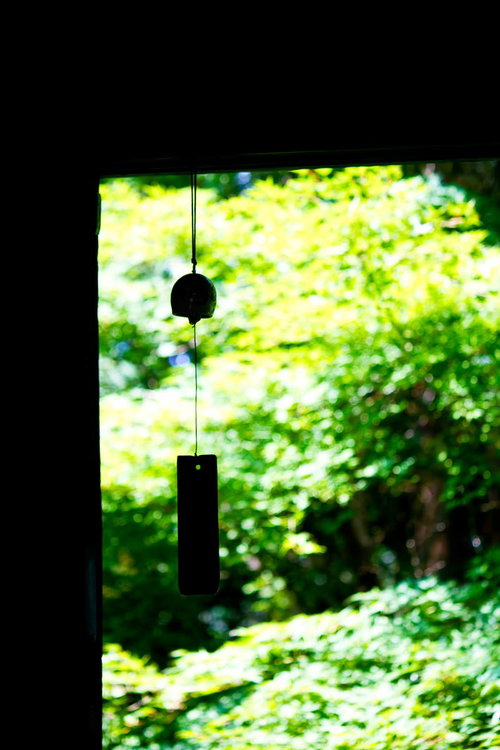 窓越しの緑の庭に浮かぶ風鈴の黒いシルエット