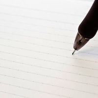 横線入りノートの紙面にペン先が触れる瞬間の写真