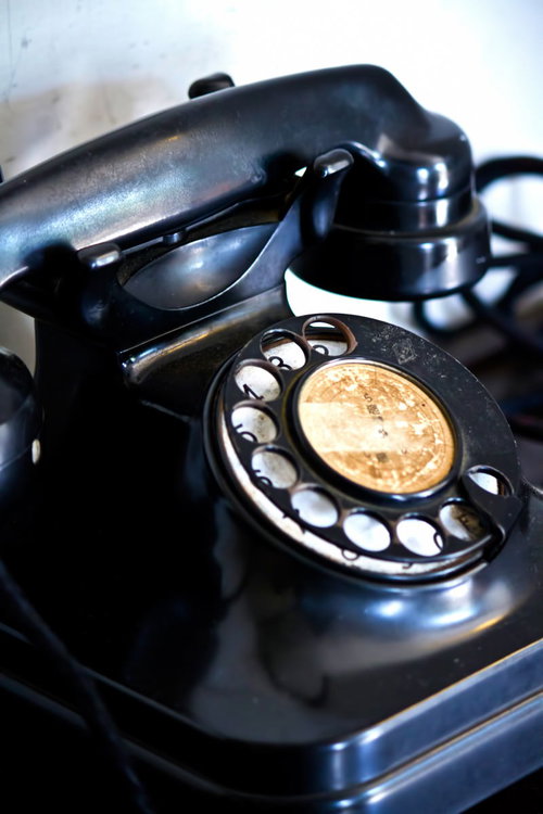 受話器が外れた白い壁の前のレトロな黒い回転式電話