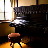 丸い椅子が置かれた窓際の黒い古いアップライトピアノの写真