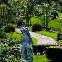 子どもの石像とアーチが続くバラ園の庭園の写真