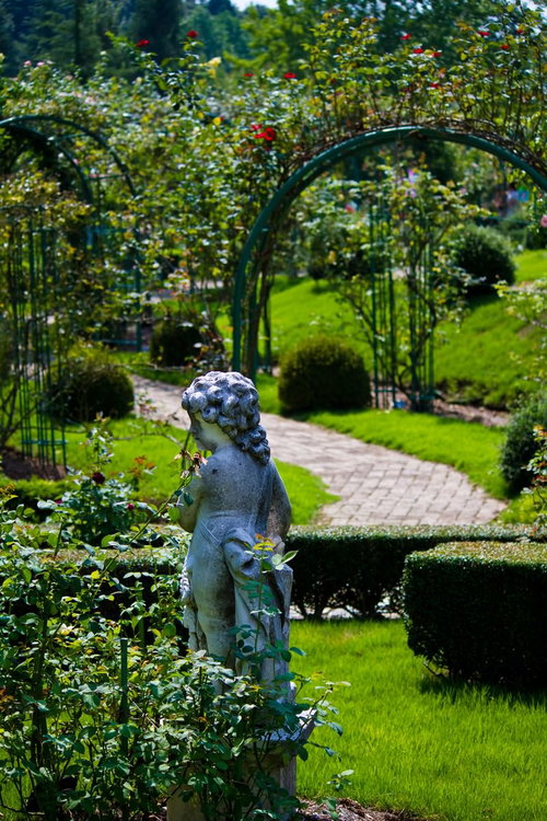 子どもの石像とアーチが続くバラ園の庭園