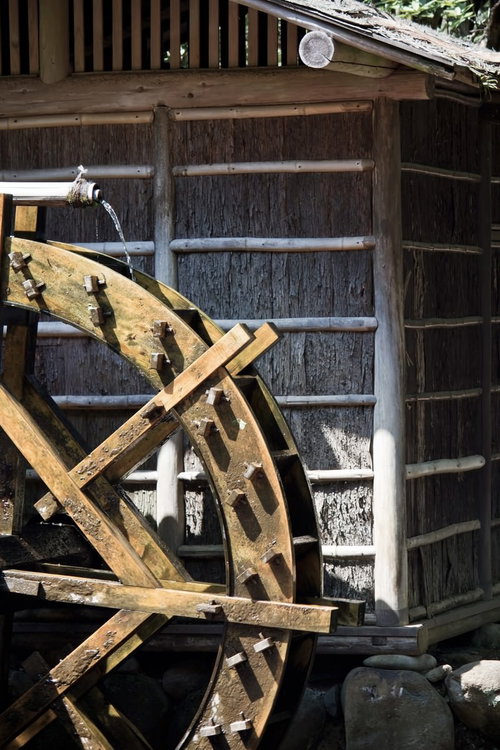古い木造建築の脇で水が流れ落ちる木製の水車小屋