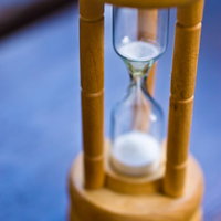 青紫色の背景に浮かぶ木製支柱の白い砂時計の写真