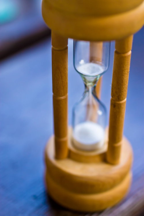 青紫色の背景に浮かぶ木製支柱の白い砂時計