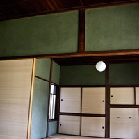 丸い照明と緑の壁が見える畳と襖の和室の写真