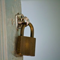 白と青緑の塗装が剥がれた古い扉の金色の南京錠の写真