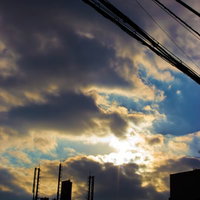 雲の切れ間から光が差す夕暮れの空と電線のシルエットの写真
