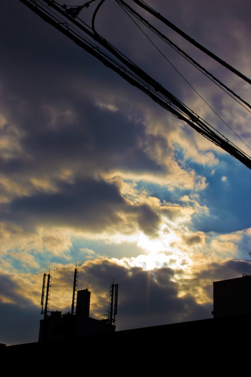 雲の切れ間から光が差す夕暮れの空と電線のシルエット