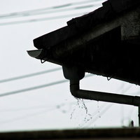 曇り空の下で雨どいからしたたる雨水の写真