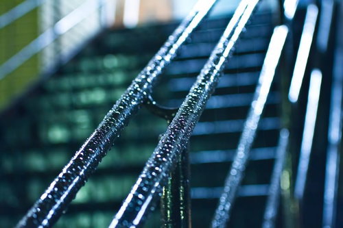 雨粒が付いた青緑色の金属手すりと緑のぼけ