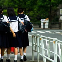 緑の並木道を歩くセーラー服の下校中の女子中学生の写真