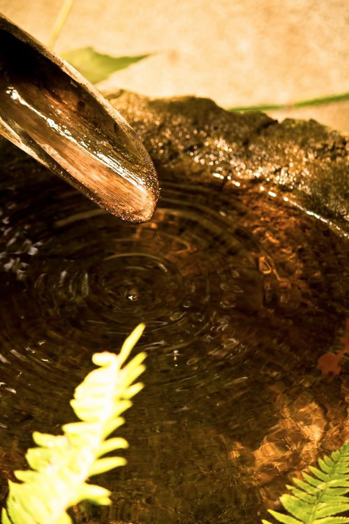 竹の柄杓から石の器に注ぐ水面の波紋