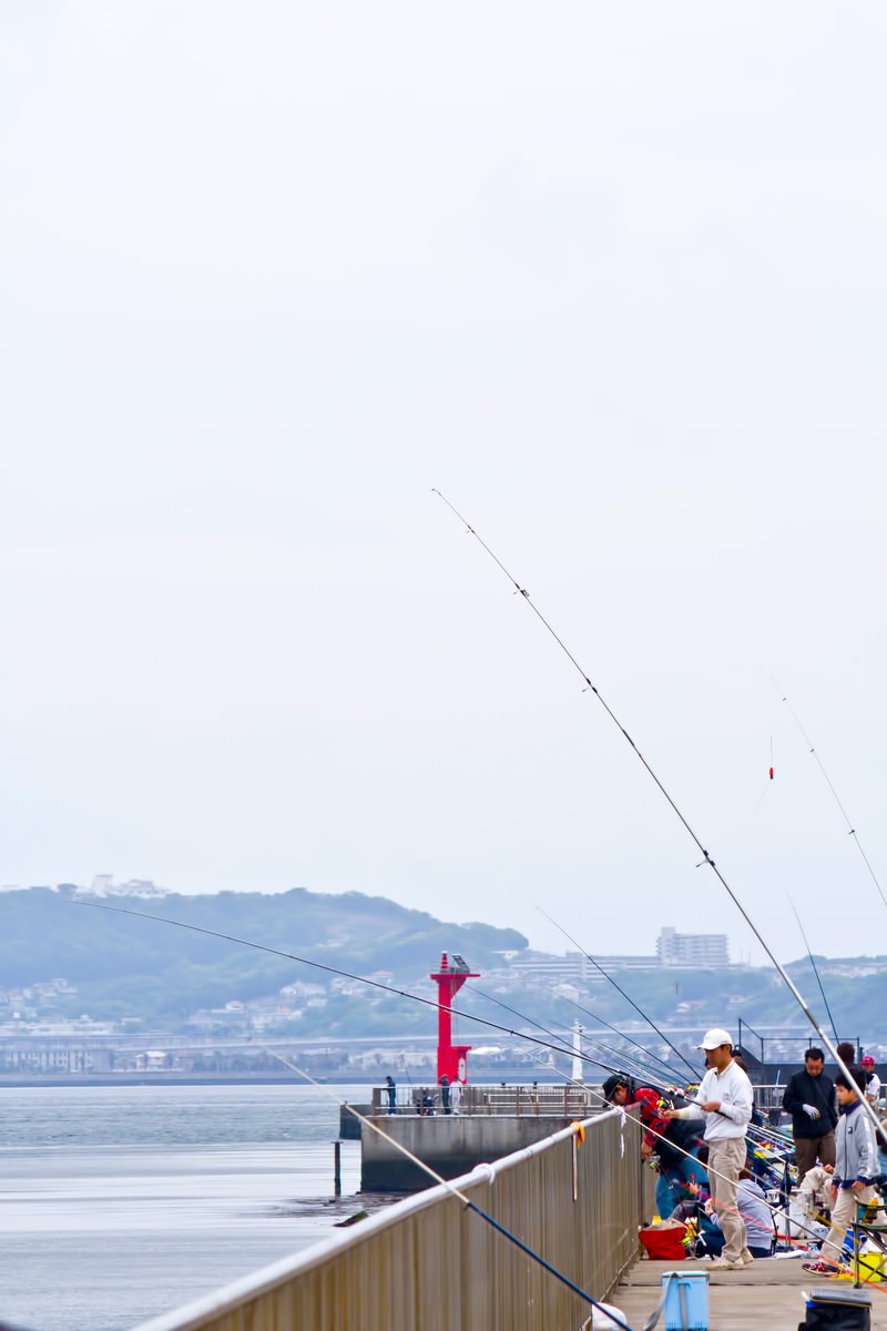 海辺の釣り場で釣りをする人々と赤い灯台