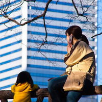 高層ビルを背に柵に座って街を眺める親子の写真