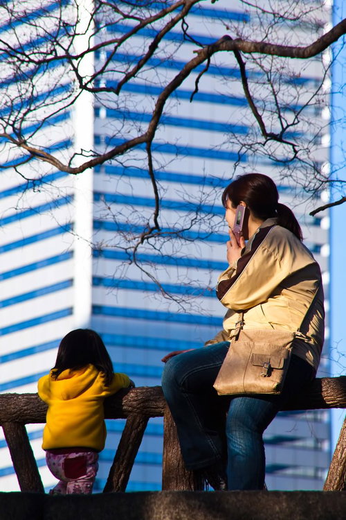 高層ビルを背に柵に座って街を眺める親子