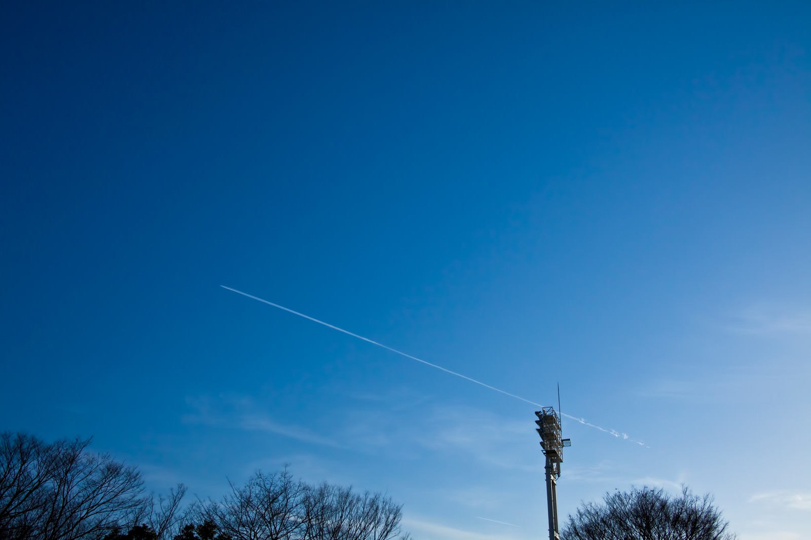 青空に伸びる飛行機雲と灰色の通信塔