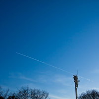 青空に伸びる飛行機雲と通信塔の写真
