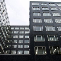 曇り空に見上げる同じ窓が並ぶ黒いオフィスビル群の写真