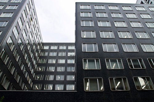 曇り空に見上げる同じ窓が並ぶ黒いオフィスビル群
