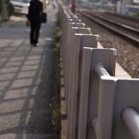 線路沿いを歩くサラリーマンと金属製フェンスの写真
