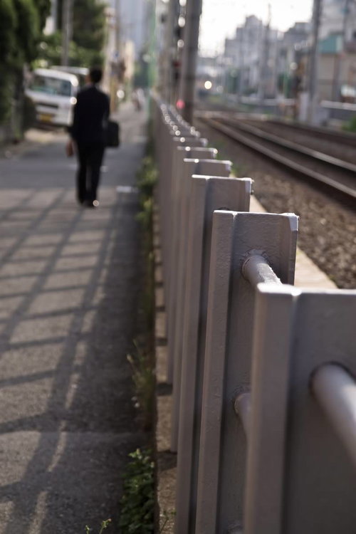 線路沿いを歩くサラリーマンと金属製フェンス