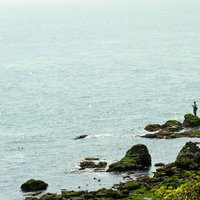 苔の生えた岩場で釣りをする人と漁船の写真