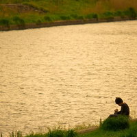 金色の水面と夕暮れの河川敷に座る人の写真