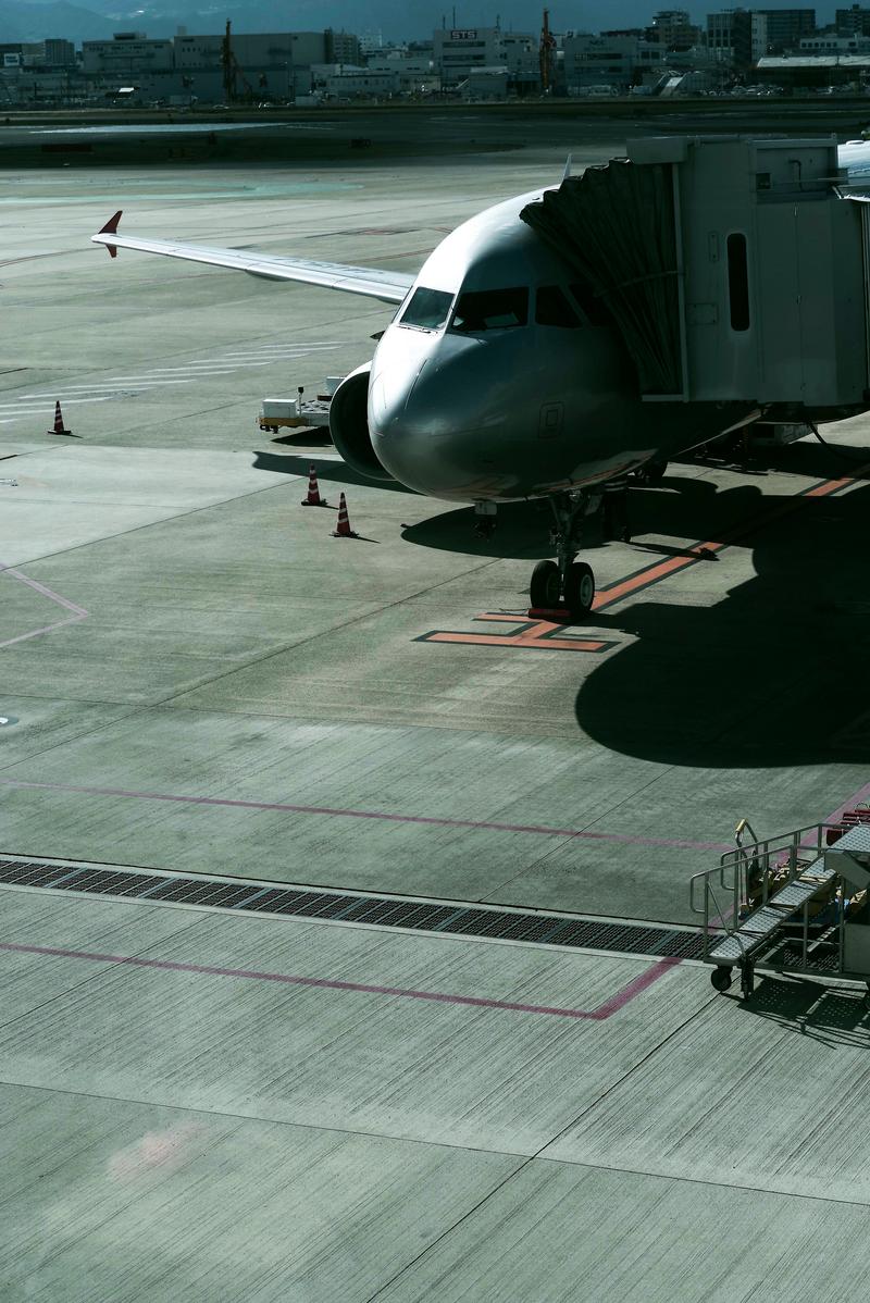 空港の駐機場に停められ、ボーディングブリッジが接続された白い旅客機