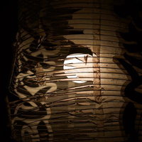 破れた和紙の隙間から光が漏れる古びた提灯の写真